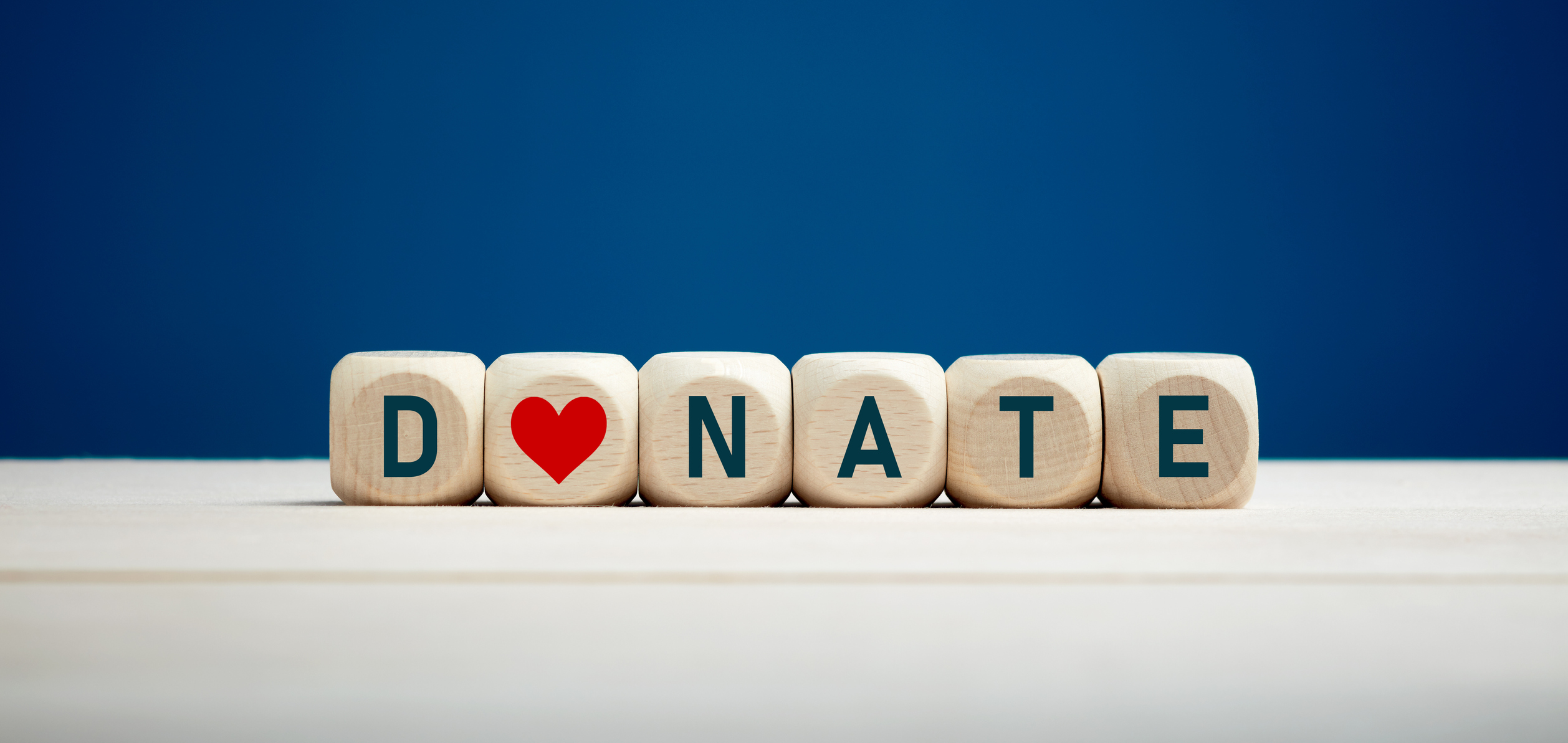 The word donate on wooden blocks with heart icon against blue background.